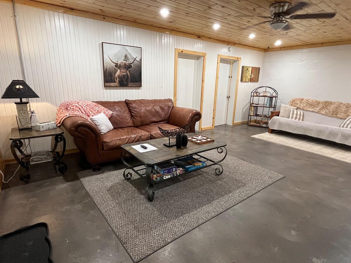 ¡Acogedora sala con encanto rústico! Cuenta con un sofá de cuero, TV de pantalla plana y techos con paneles de madera. Los grandes ventanales ofrecen unas vistas impresionantes de árboles y bosques, llenando el espacio con luz natural. 