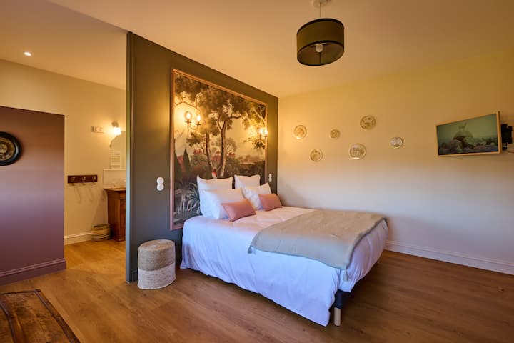 The “Entre Cœur” bedroom, measuring 22.5 sqm (242 sq. ft.), offers a cozy atmosphere thanks to its wallpaper. Facing north, it captivates with its charm and coolness. Its bathroom features an old dresser repurposed as a vanity.