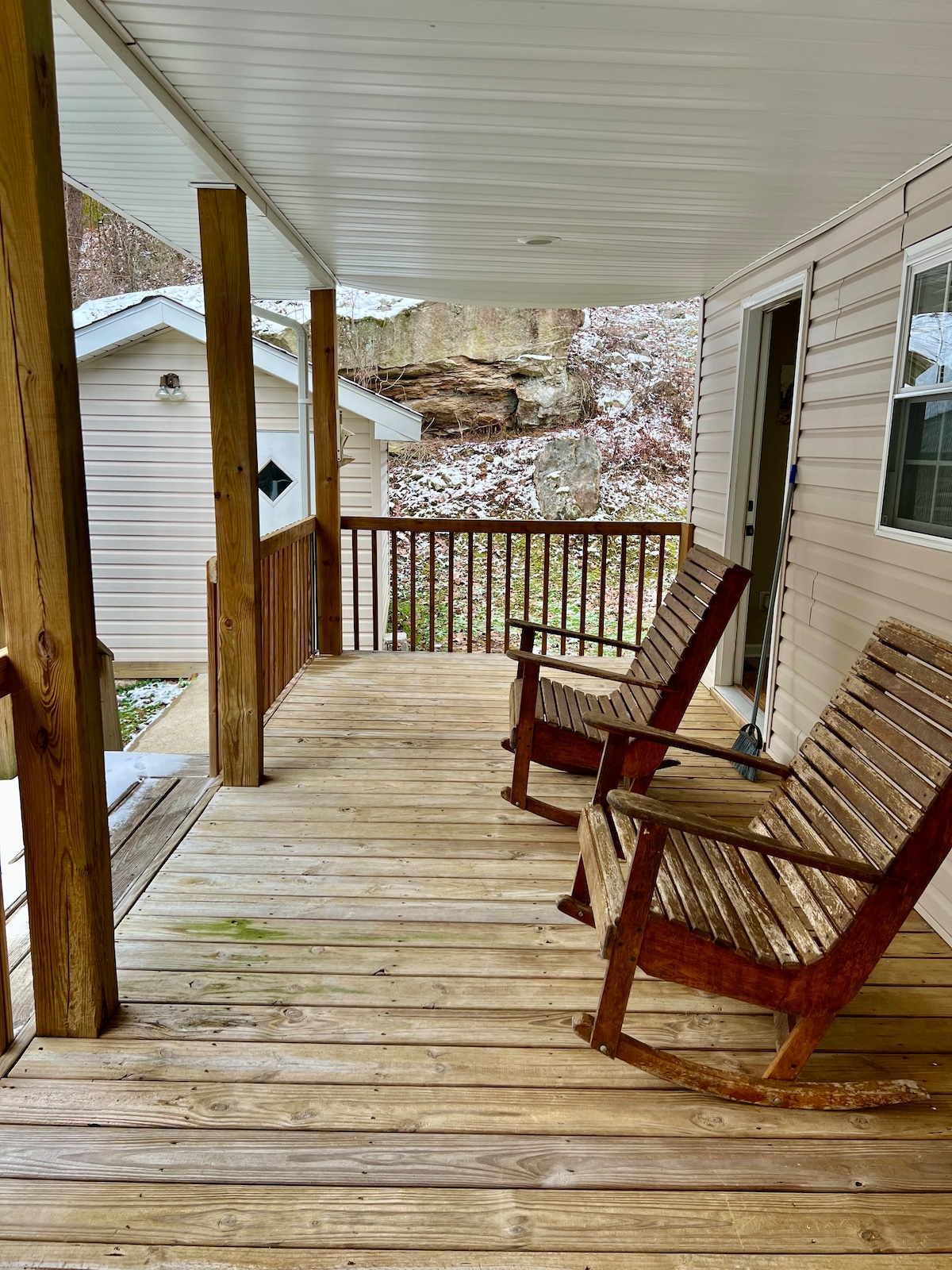 A wooden porch features two rustic rocking chairs, providing a spot to relax. The porch overlooks a tranquil setting with natural surroundings. A small outbuilding can be seen in the background, adding to the charm of the outdoor space.