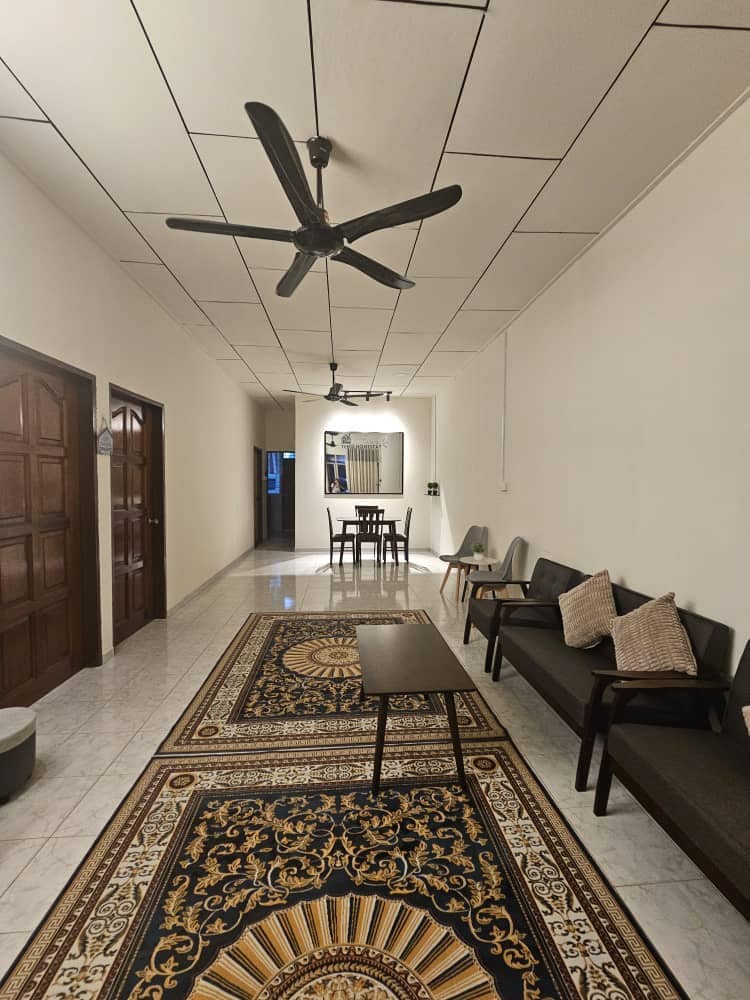 A long hallway is lined with smooth marble flooring, featuring a decorative area rug. Two ceiling fans are mounted above. On one side, a seating arrangement includes dark chairs and a coffee table, while a small dining set is visible at the far end.