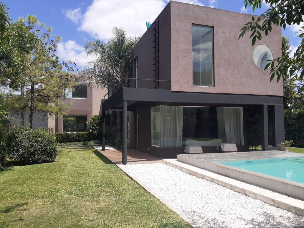 The modern house is presented in a garden setting, featuring large windows that allow natural light to enhance the interior. A spacious deck leads to a pool surrounded by neatly landscaped grass and trees, creating a serene outdoor retreat.