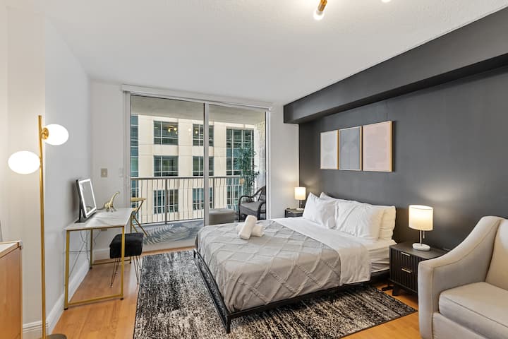 Rest in style in this modern bedroom featuring a plush queen bed with crisp white linens. A bold charcoal accent wall, designer bedside lighting, and a soft textured rug create a sophisticated and cozy atmosphere.