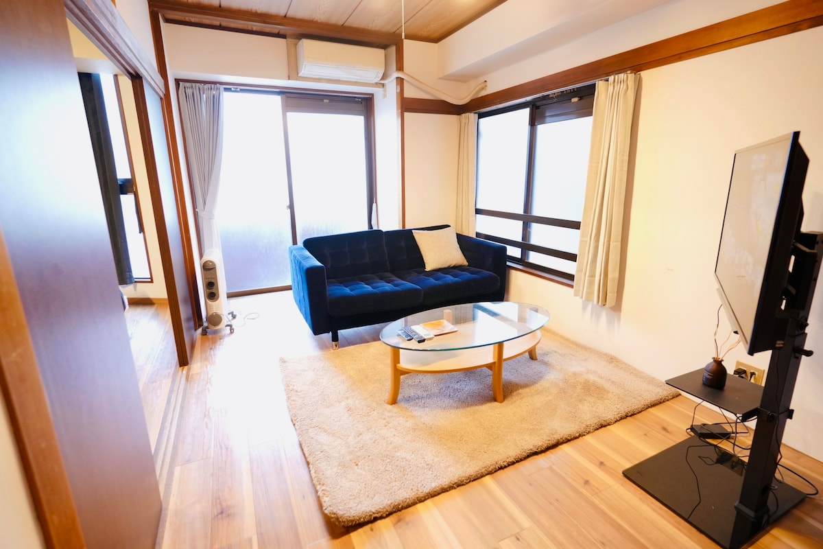 A spacious living area features a large blue sofa and a round coffee table atop a soft area rug. Two sliding glass doors provide natural light and connect to the balcony. A television is positioned on a stand in the corner, enhancing the inviting atmosphere.