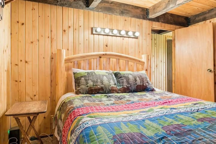 Queen bed featuring a rustic wood walls, and warm ambient lighting.