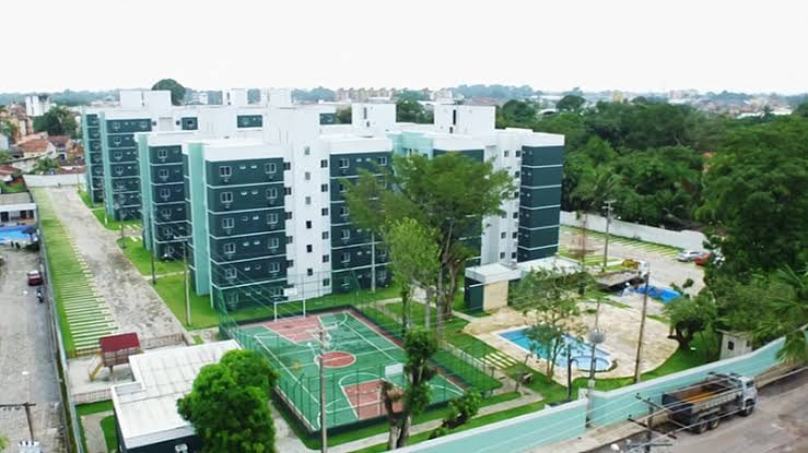 Aerial view of a modern condominium complex showcasing multiple buildings surrounded by green trees. A well-maintained outdoor area features a sports court and a swimming pool, providing recreational opportunities. The layout is organized and visually appealing, reflecting a vibrant community setting.