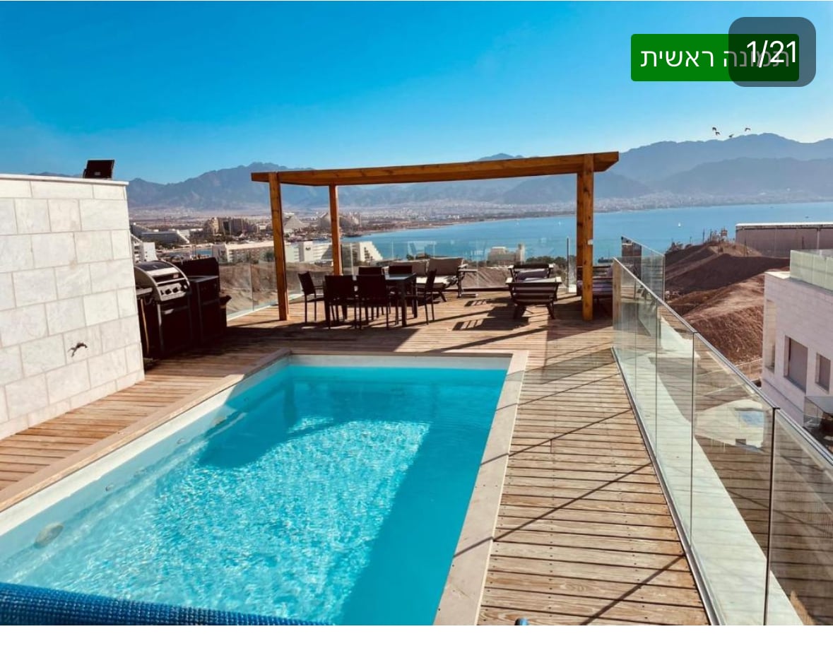 A private heated pool is situated on a spacious wooden deck, offering panoramic views of the surrounding landscape. Outdoor seating is arranged under a wooden pergola, complemented by a barbecue grill, creating an inviting space for relaxation and gatherings.