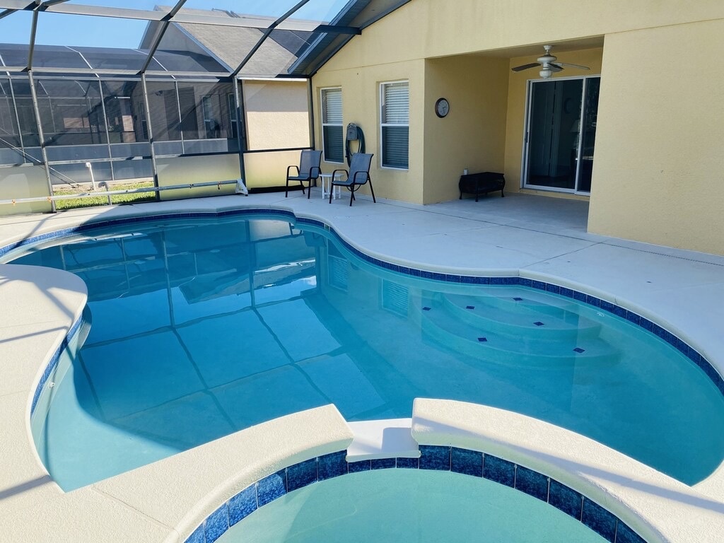 An inviting outdoor space features a private pool with a built-in spa, both surrounded by a spacious lanai. The clear water reflects the blue sky above. Two lounge chairs are situated nearby, offering a relaxed area for guests to enjoy.