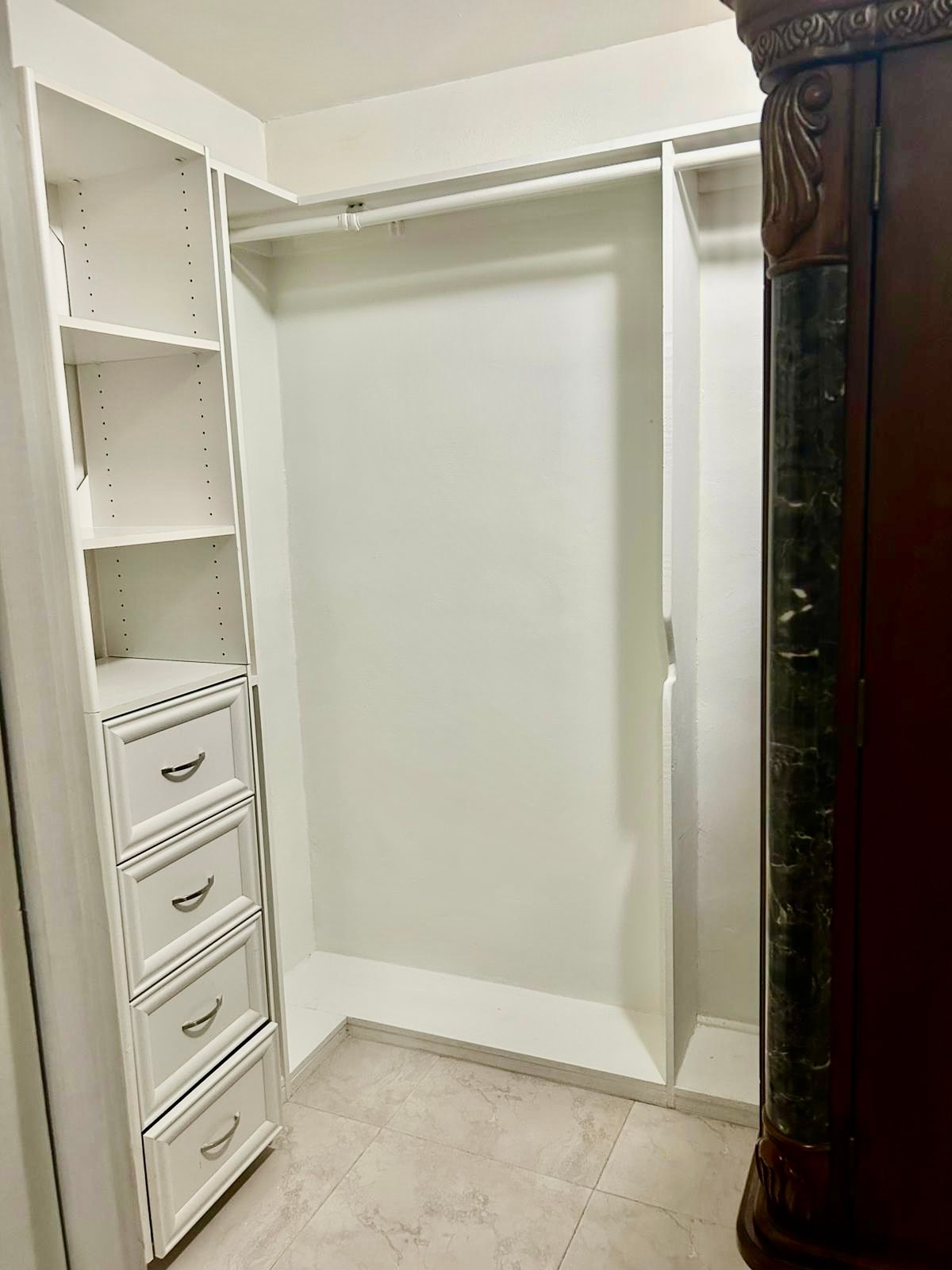 A closet space is presented with built-in shelving and drawers. The left side showcases five drawers, while an open hanging area is available on the right. The walls and shelves are painted white, creating a clean and simple storage solution.