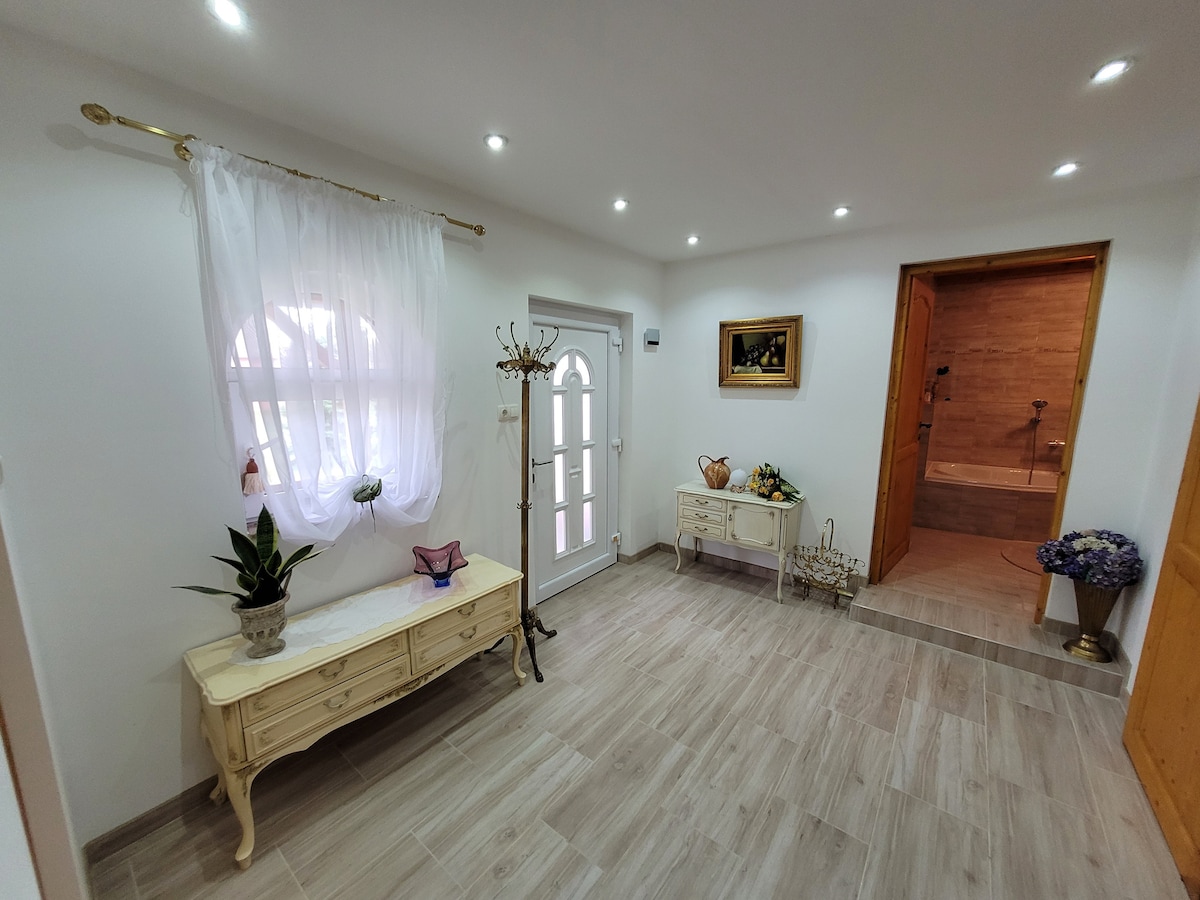 A welcoming entryway features light wood flooring and soft, neutral walls. A large window provides natural light, while a charming white console table holds decorative items. A small plant adds a touch of greenery, and the adjacent doorway leads to a well-lit bathroom.
