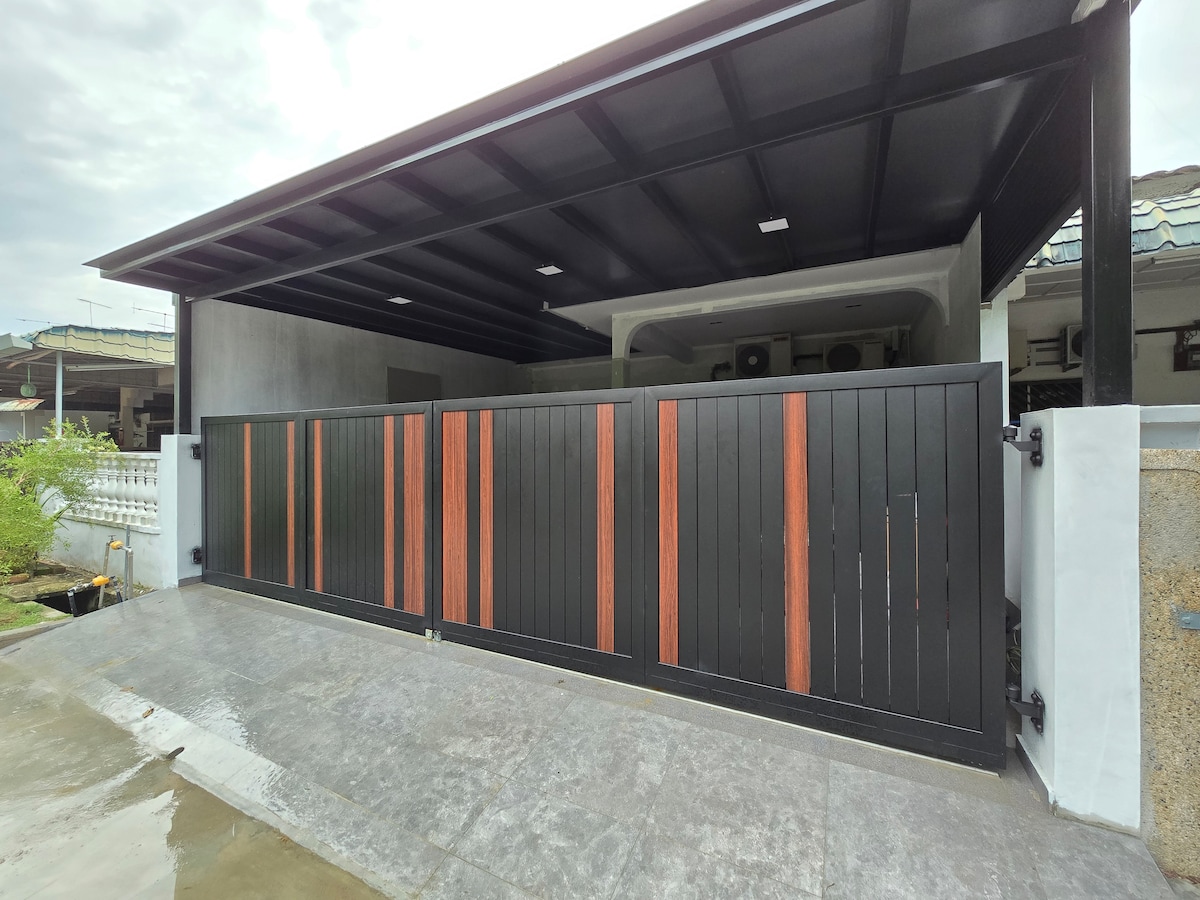 A modern garage with a sleek black fence featuring horizontal slats highlighted by wooden accents. The concrete driveway leads up to the covered parking area, offering protection from the elements. The surrounding space includes greenery, creating a welcoming entrance.