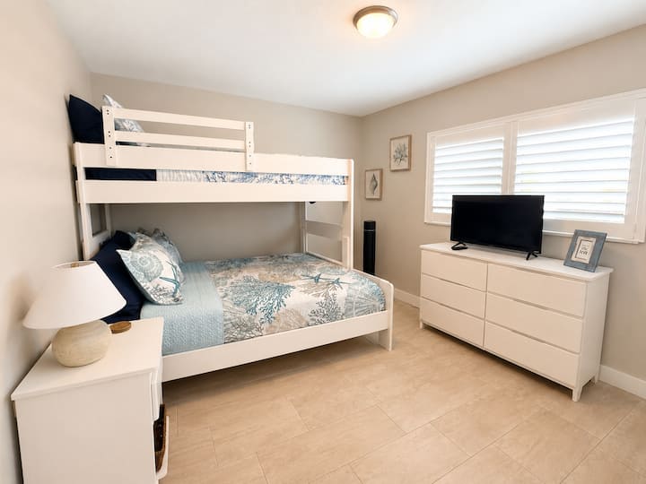 Chambre d'amis avec lit superposé simple au-dessus d'un grand lit et téléviseur intelligent