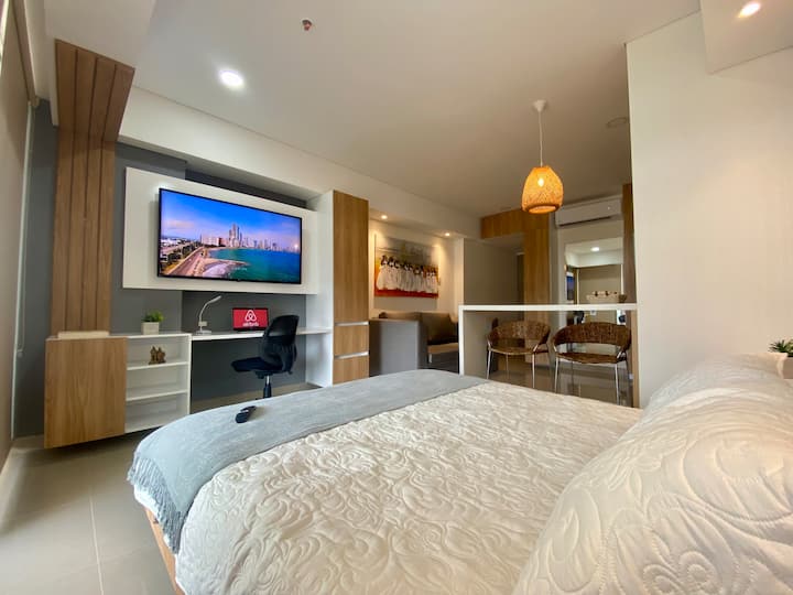 Suite con diseño moderno que integra descanso y entretenimiento: cama Queen, smart TV, zona de trabajo, barra comedor y un cómodo sofá. Ideal para disfrutar de confort y estilo en Cartagena, con todo lo necesario para una estadía perfecta.