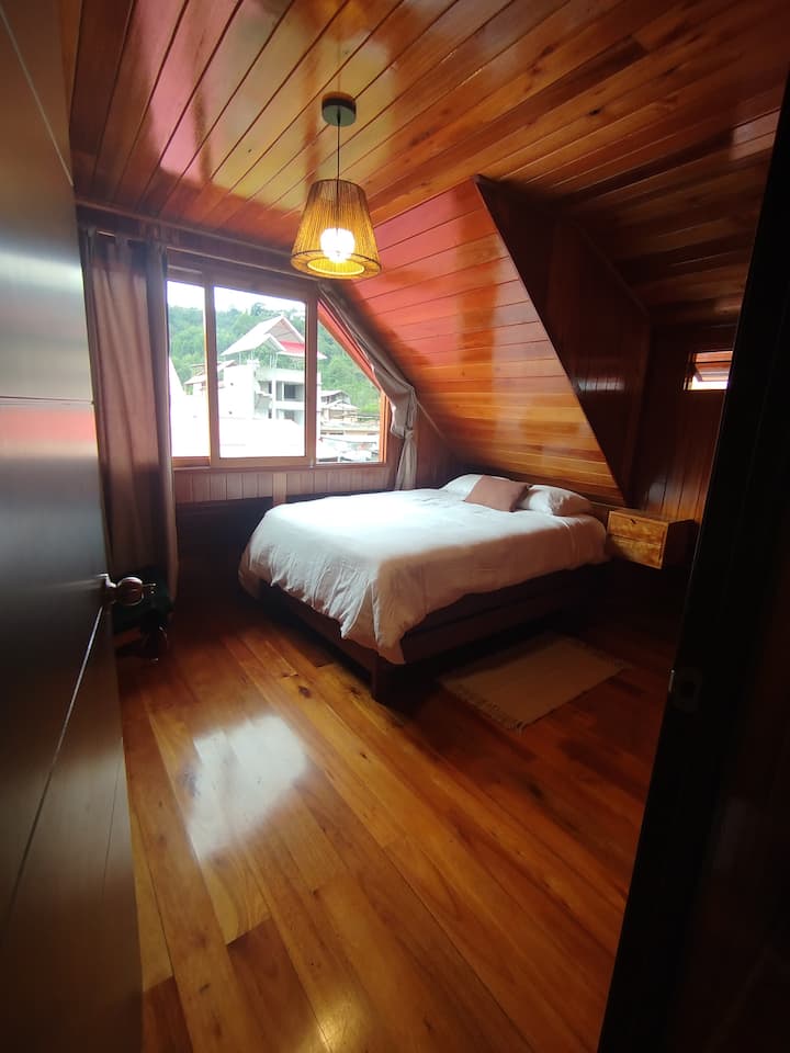 Habitación de madera con cama matrimonial, sofa y colgadores para ropa, vista paisaje cafetalero.
ubicada en el segundo nivel de la casa.