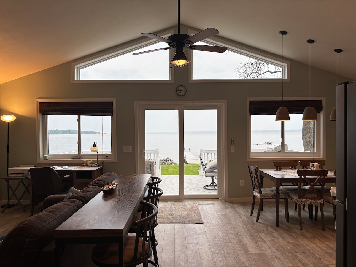 Vista desde el pasillo de entrada de los ventanales con vistas al lago. La sala de estar de planta abierta está conectada a la cocina, el comedor y el espacio de trabajo. Recientemente se ha añadido una mesa de bar detrás del sofá con sillas giratorias para 3 personas. 