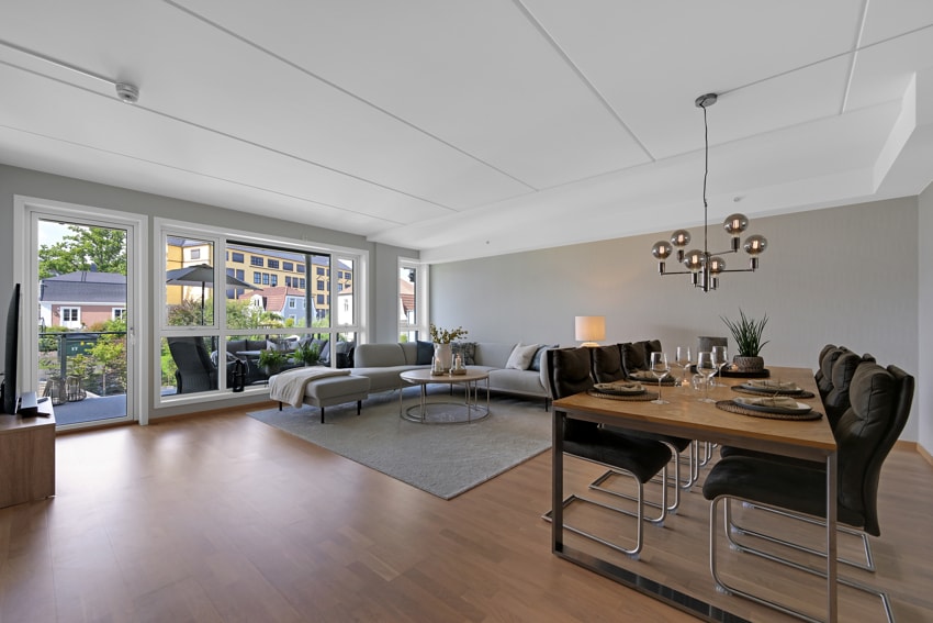 An open living and dining area features large windows offering natural light and a view of the surrounding landscape. A modern dining table is set with dinnerware, while comfortable seating is arranged in the lounge area, providing ample space for relaxation.