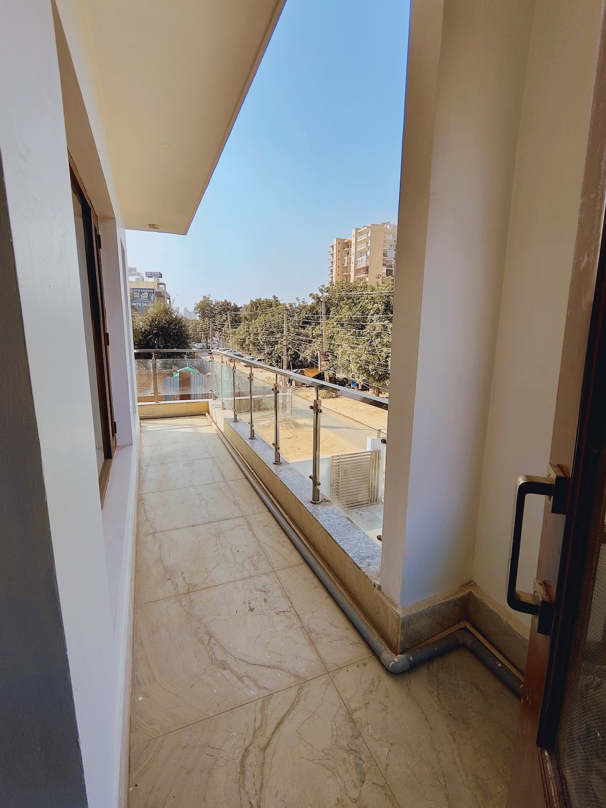 An exclusive attached terrace is visible, featuring a glass railing that offers unobstructed views of the surrounding area. The floor is finished with light-colored tiles, and sunlight brightens the space, creating a serene atmosphere for relaxation.