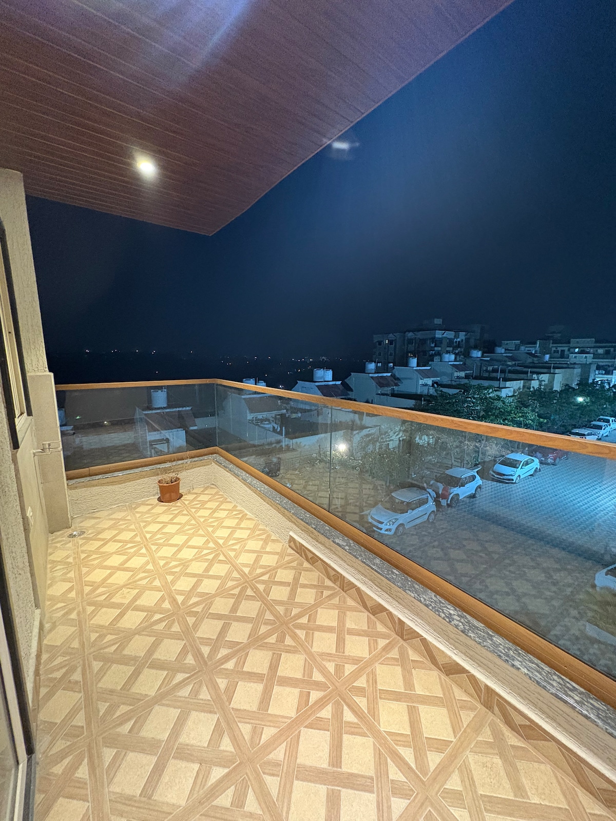 A private balcony features tiled flooring with a geometric pattern, offering unobstructed views of the surrounding area at night. Soft lighting illuminates the space, enhancing the peaceful ambiance. The balcony is enclosed by glass railings, providing safety while enjoying the serene environment.