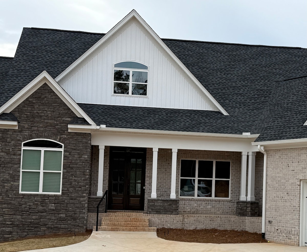 The exterior of the home features a combination of stone and siding, highlighted by a triangular gable. Large windows allow natural light to enter, and the front porch is accessible by a small set of steps, leading to double doors.