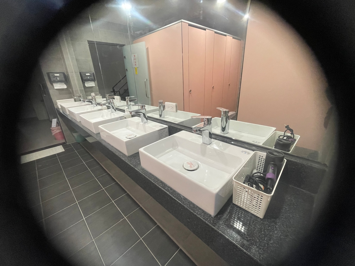 A spacious bathroom area is equipped with multiple sinks arranged in a line. Each sink features a modern faucet and a small soap dispenser. The countertop is made of dark granite, while ample storage cabinets can be seen in the background, enhancing functionality.