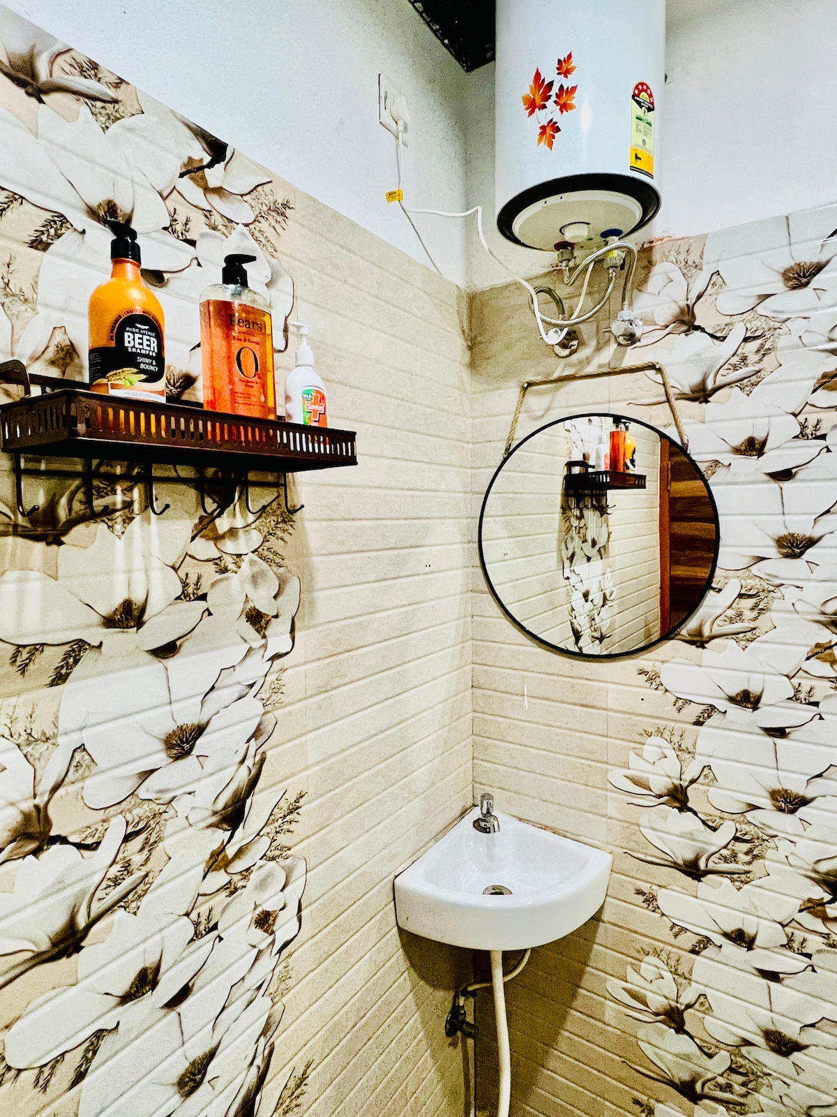 A compact bathroom area is showcased with floral-patterned walls and a circular mirror. Shelves display various toiletries, while a small sink is positioned below. A water heater is mounted on the wall above, contributing to the functional design.