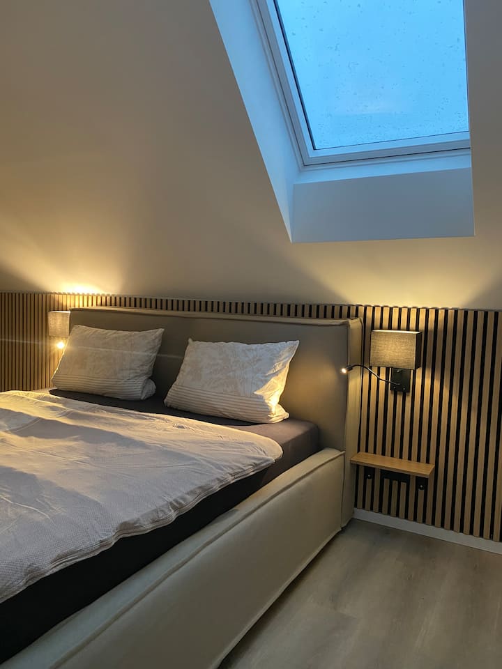 מיטת קפיצים, מנורת קיר עם מנורת קריאה נוספת, שני חלונות גג עם שערי עידון, שידות ליד המיטה לאחסון, ארון בגדים ושולחן קונסולה מובנה לשימוש כאזור עבודה או שולחן הלבשה.