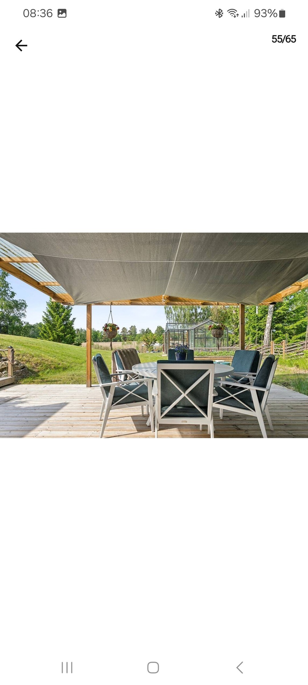 An outdoor dining area is featured under a shaded canopy. A rectangular dining table is surrounded by six cushioned chairs. Lush greenery is visible in the background, complementing the serene setting.