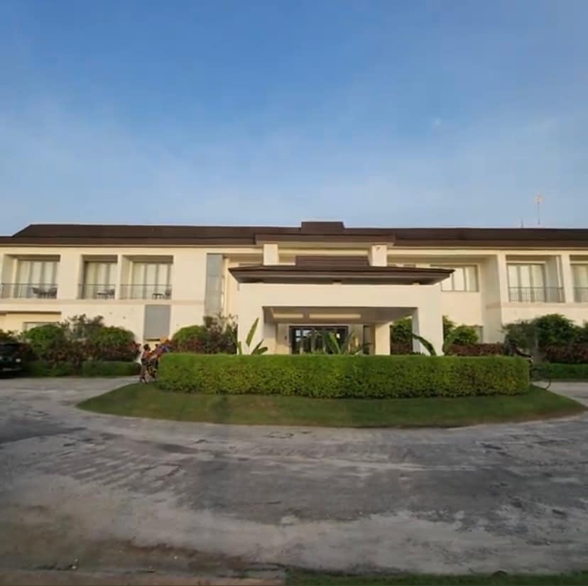 The exterior of a three-bedroom duplex is presented, featuring a well-maintained façade with large windows. Surrounded by manicured greenery, the property includes a circular driveway, with ample space for parking. The sky above is clear, contributing to a serene atmosphere.