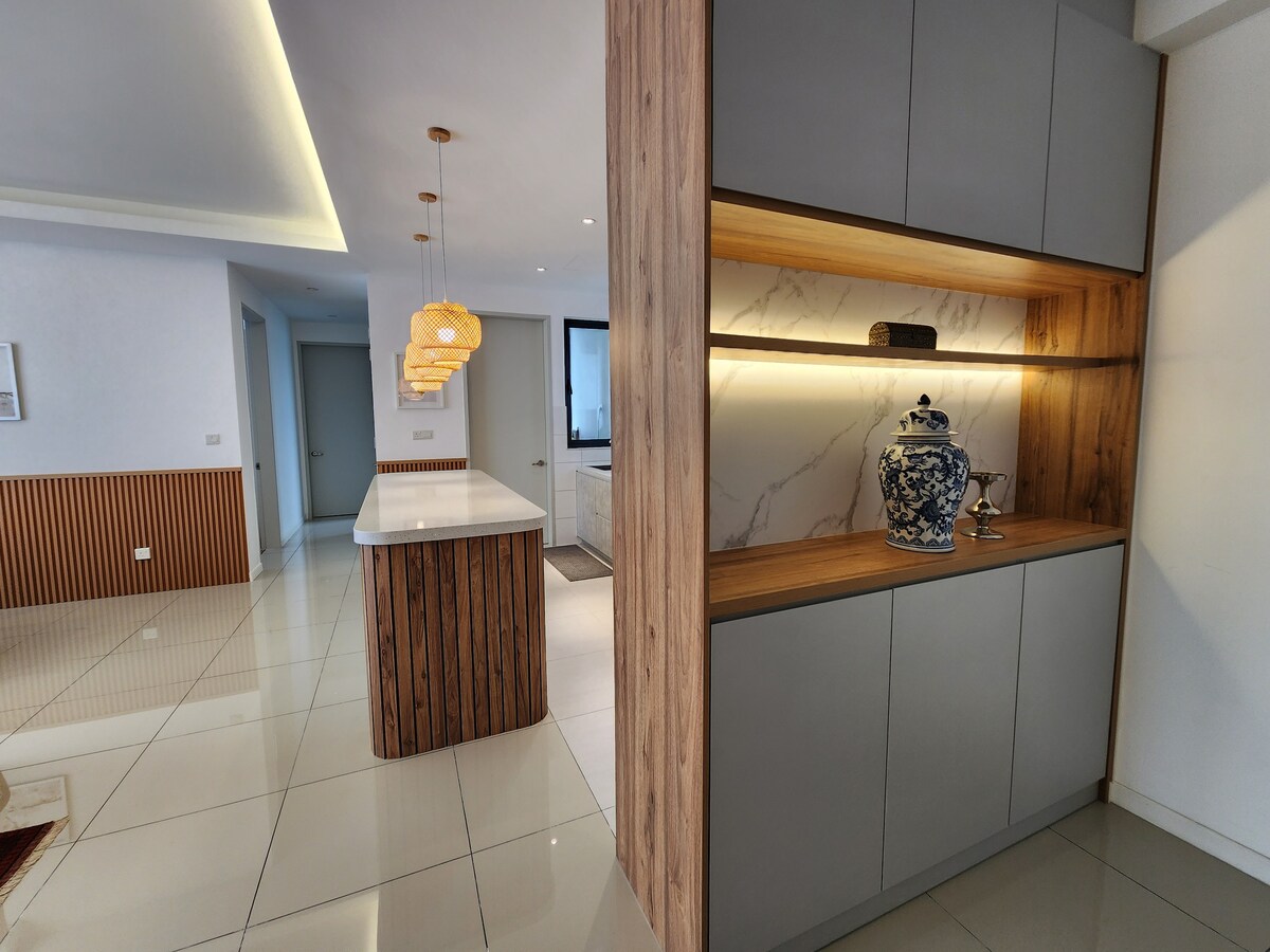 A contemporary kitchen space is highlighted, featuring a sleek island with a smooth white countertop. The cabinetry combines natural wood and gray finishes. A decorative blue and white vase is displayed on the shelf, complemented by soft, warm lighting that enhances the room's elegance.