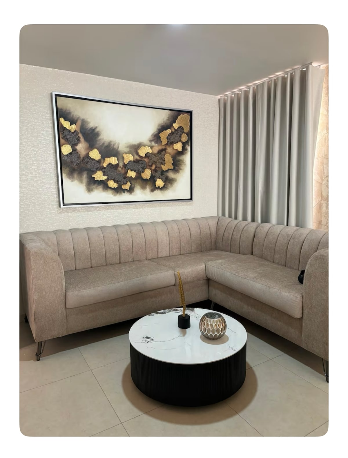 A corner seating area is featured with a plush, light-toned sectional sofa, complemented by a round coffee table. A decorative piece rests atop the table, and a large artwork with gold accents is displayed on the wall, enhancing the ambiance.