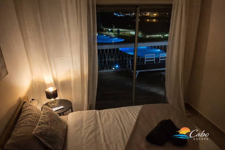 Un dormitorio tranquilo con líneas claras y una vista directa del tranquilo paisaje de la piscina nocturna y el lago.
