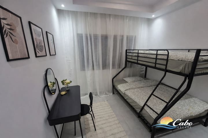 Una habitación elegante con una amplia cama baja y una cama individual arriba, complementada con un área de trabajo y maquillaje elegantemente amueblada.