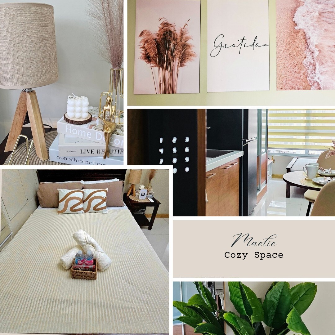 A minimalist studio space is presented, featuring a cozy double bed adorned with neutral linens and decorative pillows. On the bedside, a lamp and styled books create an inviting atmosphere. Artwork is displayed on the wall, adding a touch of elegance alongside a small dining area.