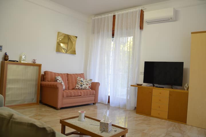 Ampio soggiorno con aria condizionata e riscaldamento a termosifoni, armadio per abiti, cassettiera, divano letto alla francese, divano letto singolo, tavolini a mosaico, comodino, Smart TV, zanzariere e tende oscuranti. Doppio accesso al terrazzo.