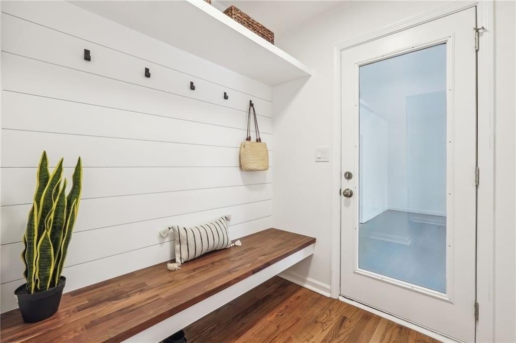 A welcoming entryway features a wooden bench against a white shiplap wall with hooks for hanging items. A small plant adds a touch of greenery, and a door with glass panels offers a view of the exterior.
