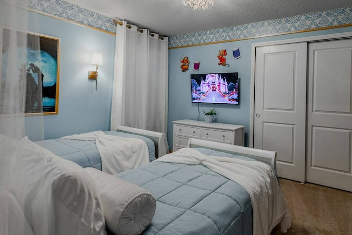 Enjoy a charming room with two cozy twin beds in soft blue linens, playful decor, and cheerful wall art. A sleek white dresser and flat-screen TV enhance your stay, while light blue walls create a refreshing atmosphere.