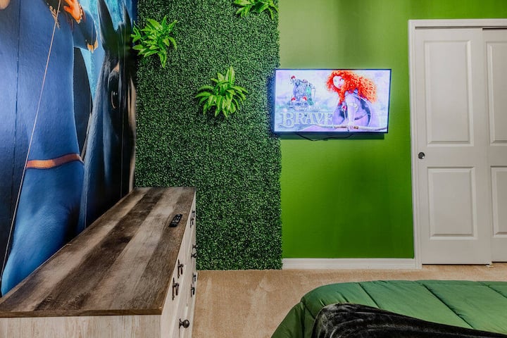 Bright green walls and stylish faux greenery make this room a lively retreat. Enjoy a cozy bed, rustic dresser, and vibrant artwork while you relax and watch your favorite shows on the wall-mounted TV.