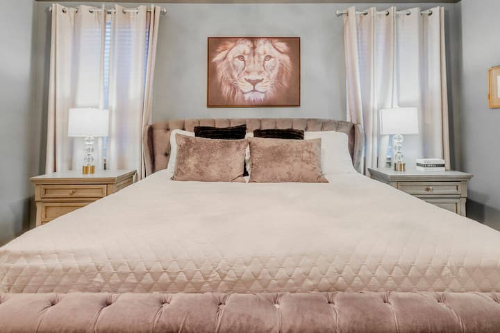 Wake up in a beautifully styled bedroom featuring a plush tufted bed with soft pastel linens and elegant pillows. Natural light fills the room, showcasing tasteful décor, including a unique lion artwork that adds character.