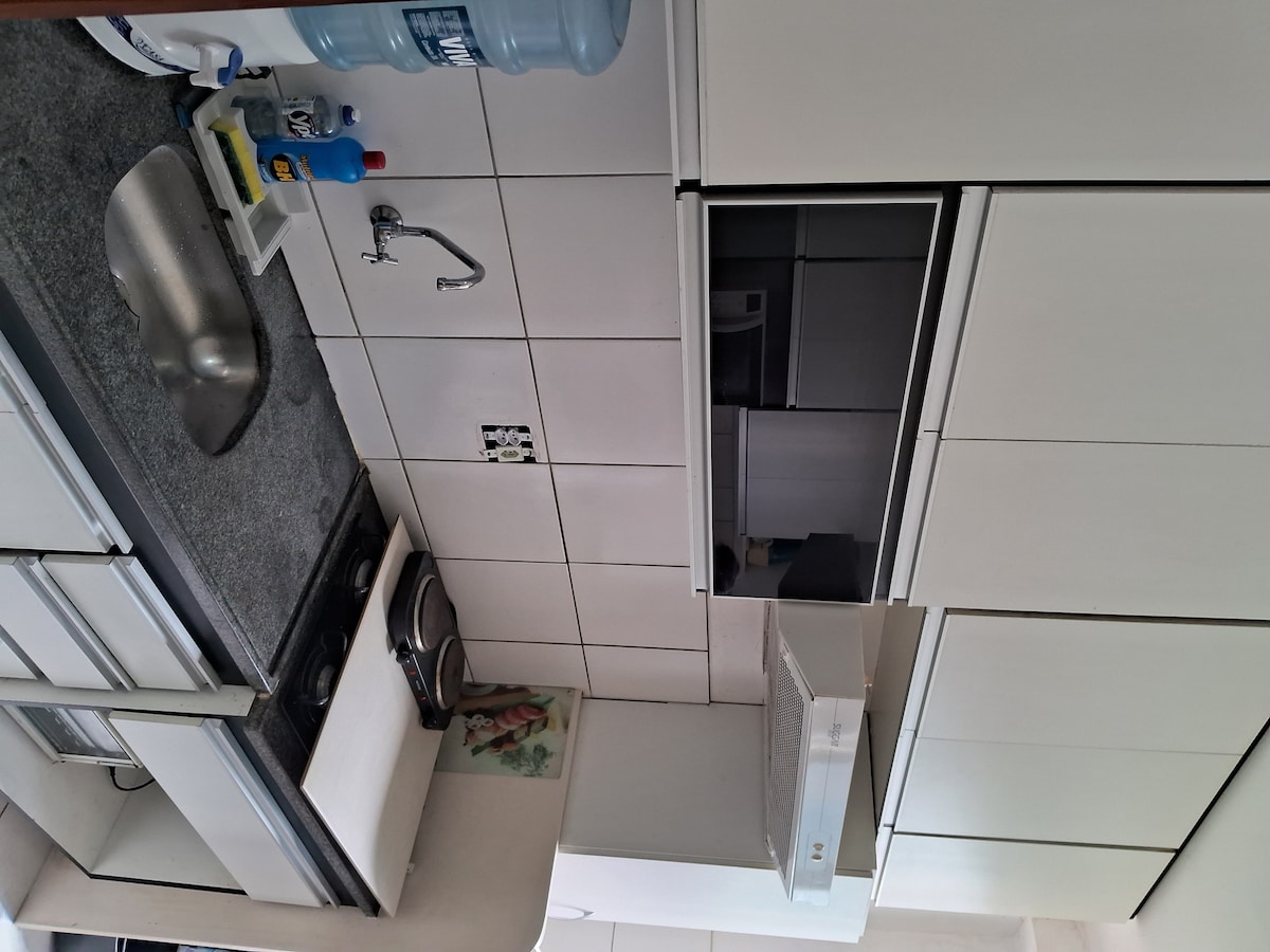 A modern kitchen features white cabinetry with sleek finishes. A double sink with a chrome faucet is set against a gray countertop. A stove and oven are visible, along with a microwave mounted above. The space includes an organized layout, providing accessibility for meal preparation.