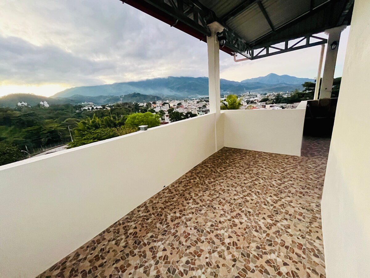 A spacious terrace is featured, furnished with a tiled floor and surrounded by low walls, providing an unobstructed view of the mountains and surrounding area. The open space suggests an ideal location for relaxation, with ample room for seating or lounging options.