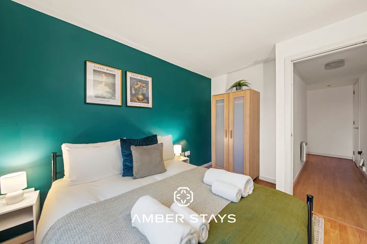 U ovoj modernoj spavaćoj sobi kombinacija je svijetlozelenkasto-plave boje na jednom zidu i svježih bijelo-zelenih tonova na posteljini. Krevet je okružen namještajem od svijetlog drva, a pogled vodi prema hodniku s drvenim podom koji je ispunjen sunčevom svjetlošću.