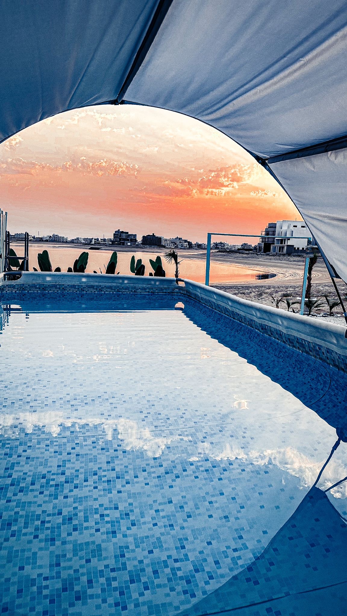 A tranquil pool reflects the soft colors of a sunset, framed by an arching canopy. The clear water glistens, inviting relaxation, while a serene view of the waterway and greenery is visible in the background.