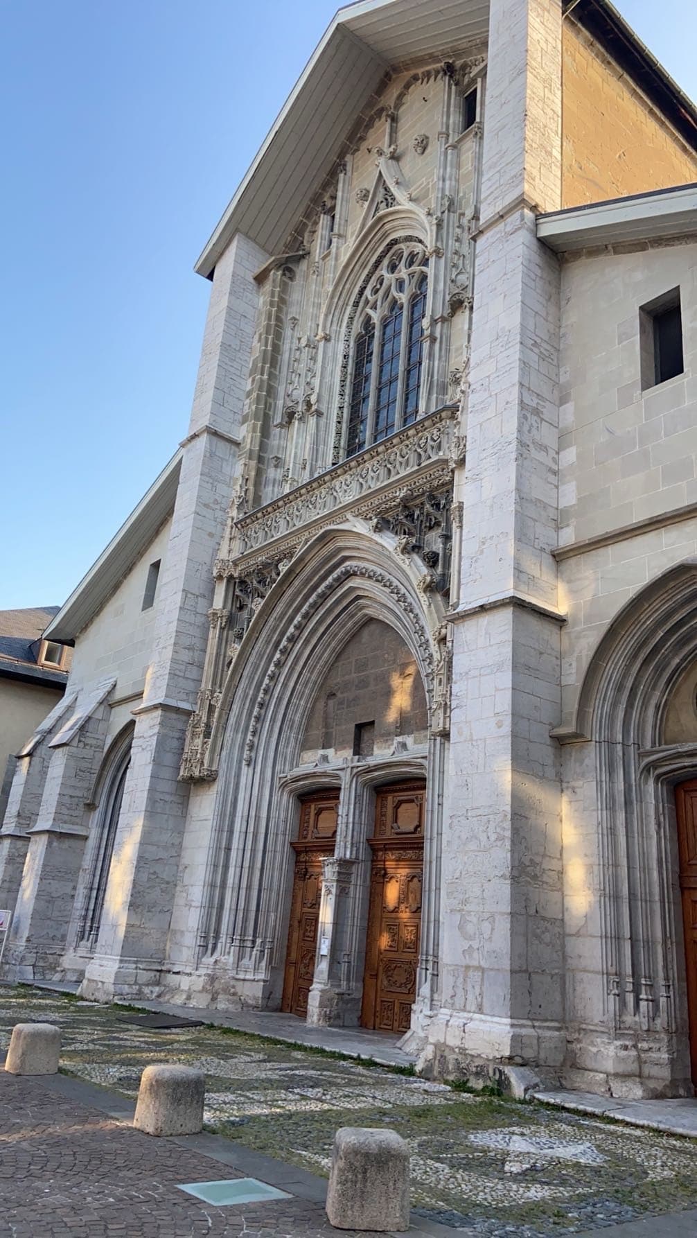 The image captures the elegant façade of a historic cathedral, showcasing intricate stonework and detailed archways. Two grand wooden doors are framed by ornate carvings, while soft sunlight highlights the textured surface of the stone, contributing to the architectural appeal.