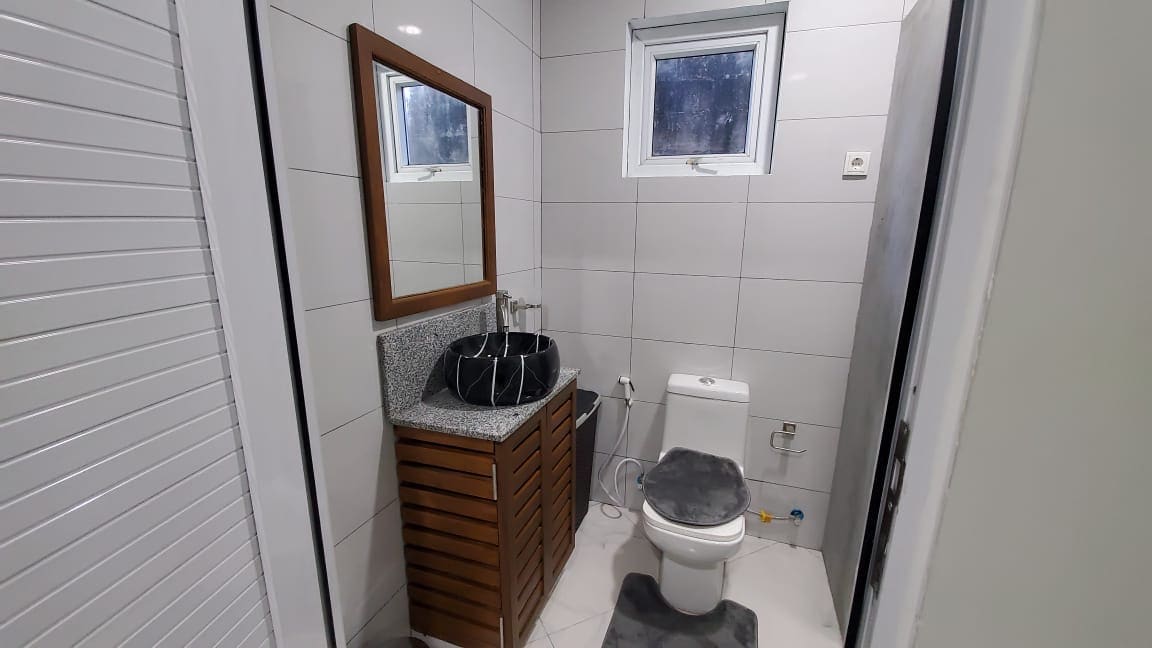 The bathroom features modern fixtures and a sleek granite countertop with a bowl sink. A wooden cabinet provides storage beneath the sink. A white toilet is positioned beside a small window, with neutral tiles covering the walls and floor, enhancing the clean aesthetic.