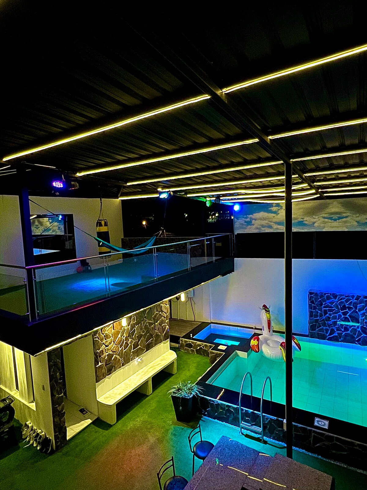 A private pool area is highlighted under soft lighting, featuring a spacious pool deck with vibrant decorations. A relaxing jacuzzi is positioned nearby, surrounded by sleek stone walls. The upper level offers a balcony view overlooking the pool, enhancing the inviting layout of the space.