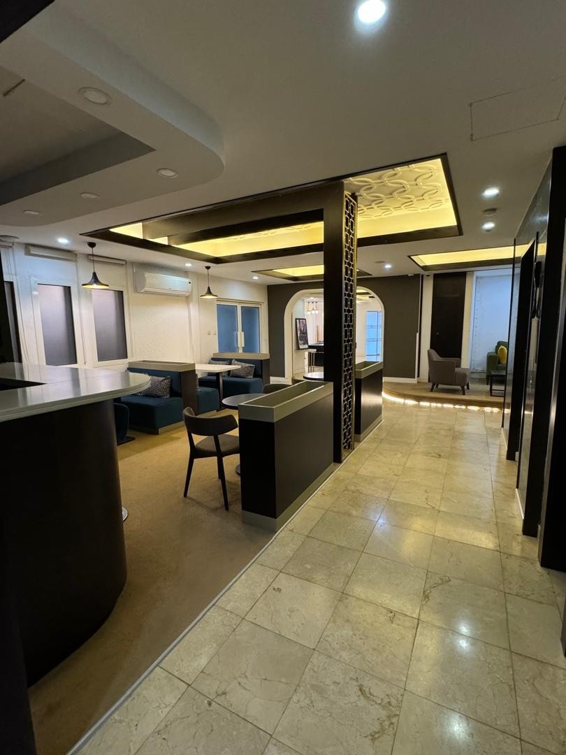An inviting hallway showcases a blend of modern and elegant design, featuring polished marble flooring. Soft lighting illuminates the space, highlighting comfortable seating arrangements and large windows that provide natural light. A partition adds a sense of privacy while maintaining an open feel.