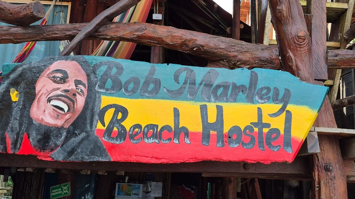 A colorful sign is prominently displayed, showcasing the name of the property. The striking design consists of bold letters painted in red, yellow, and green, framed by a rustic wooden structure. This welcoming entrance hints at a vibrant community atmosphere.
