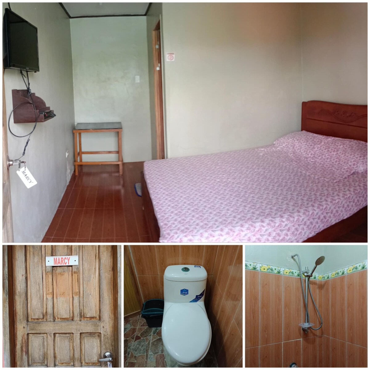 A minimalistic room features a spacious bed with a patterned pink bedspread, accompanied by a small table and a wall-mounted television. The adjoining bathroom includes a toilet and a shower area, with earthy tones and a wooden door adding to the serene ambiance.