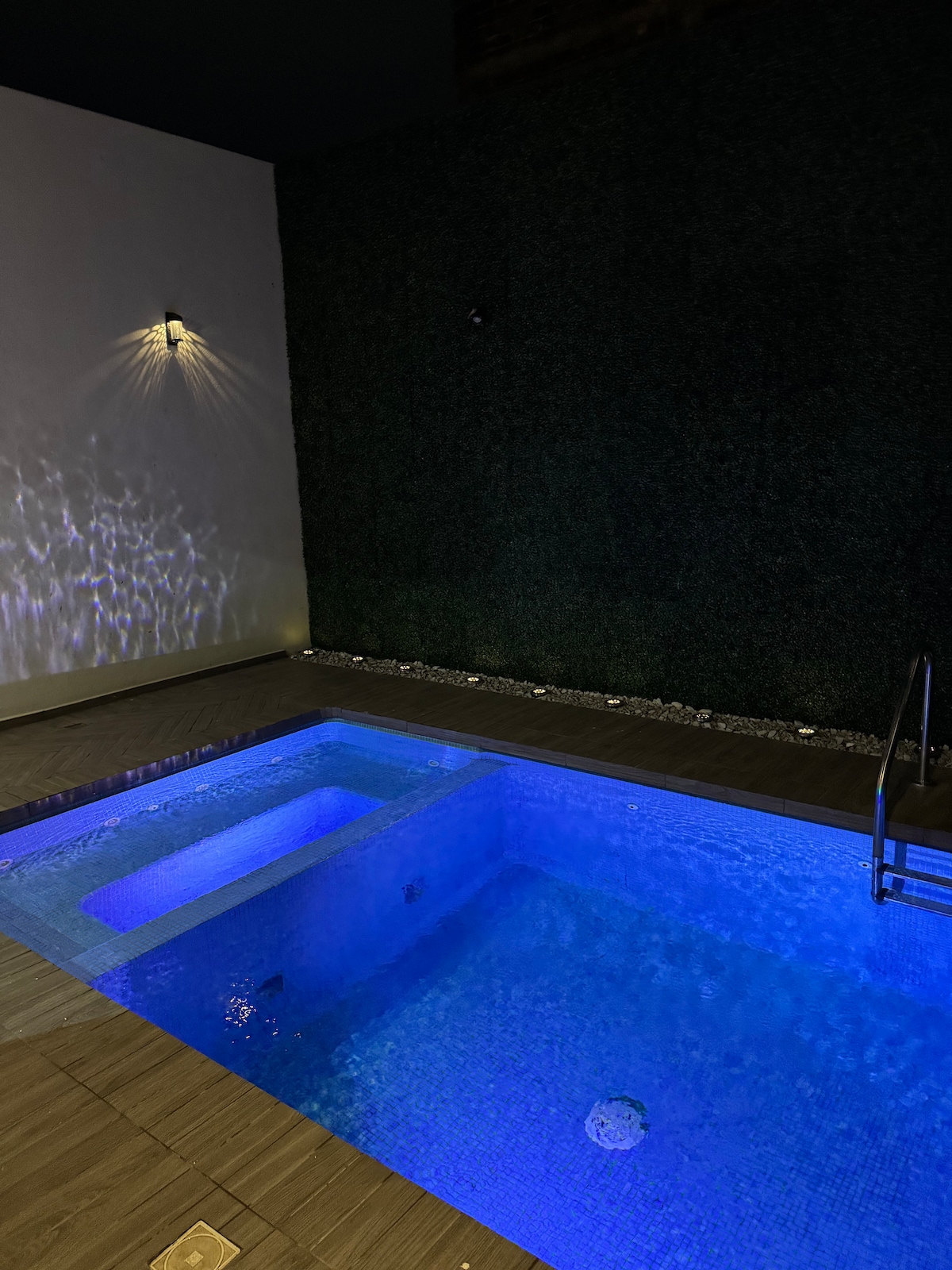 A private pool area is showcased, featuring clear blue water illuminated with soft lighting. The pool is surrounded by elegant stone flooring and a vertical garden wall, enhancing the serene ambiance.