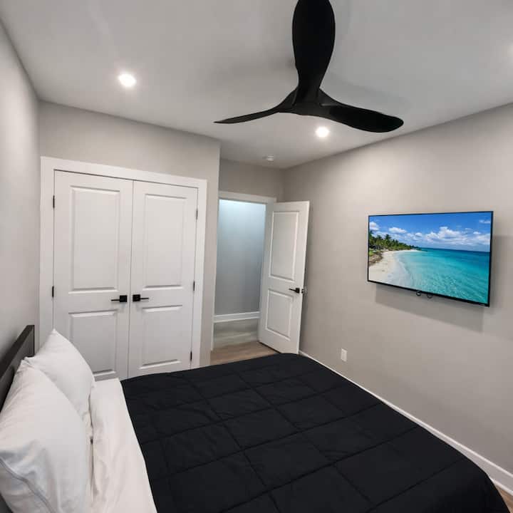 Furahia chumba cha kulala maridadi chenye kitanda aina ya queen kilicho na matandiko meupe safi, blanketi nyeusi laini, Smart TV iliyowekwa ukutani, taa zilizowekwa ndani ya ukuta na feni ya kisasa ya dari. Safi, yenye starehe na inayofaa kwa ukaaji wa kupumzika.