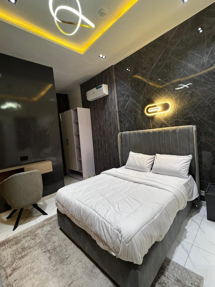 Moderna habitación doble con cama de terciopelo, iluminación LED, aire acondicionado y un espacio de trabajo dedicado. Los elegantes detalles oscuros ofrecen un refugio acogedor y elegante.